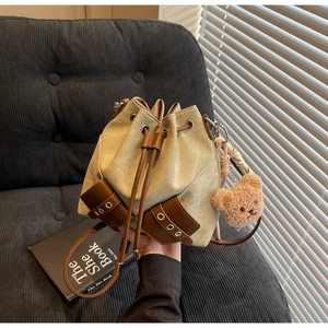 Detail einer beigen Canvas-Beuteltasche mit braunem Lederzug und Teddybär-Anhänger
