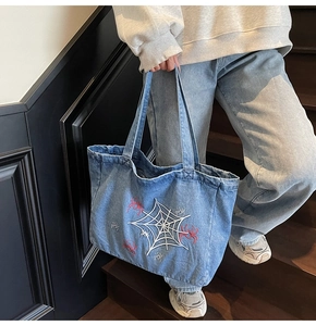 Detail der blauen Denim-Schultertasche mit weißem Spinnennetz und roter Spinnenstickerei