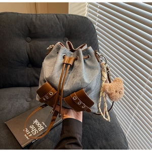 Detail der blauen Denim-Beuteltasche mit braunem Lederbesatz und süßem Bärenanhänger