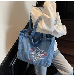 Detail einer blauen Denim-Tragetasche mit Spinnennetz-Stickerei und breitem Gurt