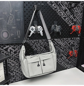 Detail of grey nylon crossbody bag with dual zippers hanging on a dark pegboard