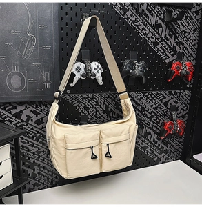 Detail view of beige crossbody bag with dual zippered pockets on black pegboard