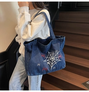 Detailaufnahme der dunkelblauen Denim-Tasche mit weißem Spinnennetz und rotem Spinnen-Stick