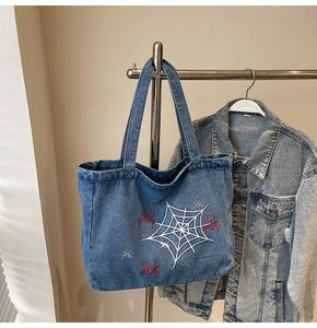 Detailansicht der Spinnennetz-Stickerei auf einer blauen Denim-Tragetasche mit roten Akzenten