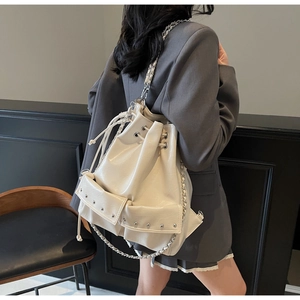 Rear view of cream bucket bag with silver chain and rivet details worn by a model