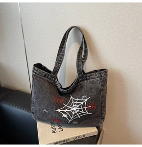 Detail der dunkelgrauen Denim-Handtasche mit weißem Spinnennetz und roter Spinnenstickerei