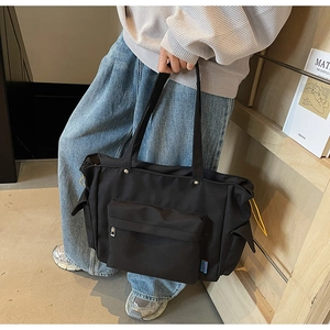 Close-up of black canvas tote bag showing large front pocket and side compartments