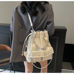 Detail of cream drawstring bucket bag with silver studs and chain straps on model