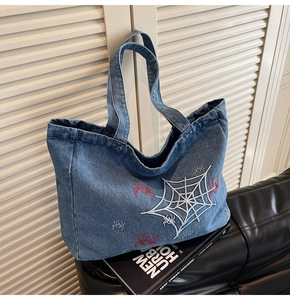 Detail der roten Spinnenstickerei und des weißen Webmusters auf blauer Denim-Tasche