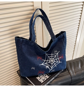 Detail einer dunkelblauen Jeans-Tote-Bag mit weißem Spinnennetz und roter Bestickung