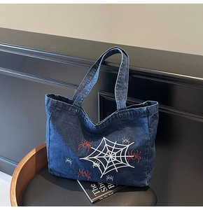 Detail der blauen Denim-Tragetasche mit weißem Spinnennetz und roter Spinnenstickerei