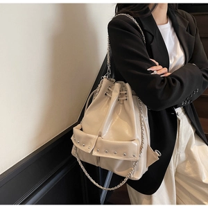 Detailed view of beige drawstring bucket bag with silver rivets and metal chain strap