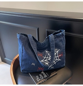 Detailansicht der Spinnen- und Netzstickerei auf einer dunkelblauen Denim-Tragetasche