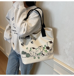 Shoulder view of white canvas tote bag with black handles and cute cartoon cat prints