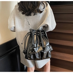Detail of black glossy bucket bag with drawstring closure and silver chain straps