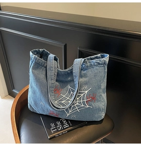 Detail einer blauen Denim-Tasche mit Spinnen-Stickerei auf schwarzem Stuhl