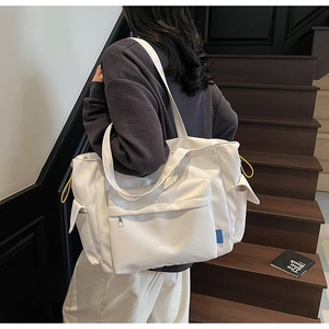 Detail of white canvas tote bag featuring large front zipper pocket and yellow drawstrings