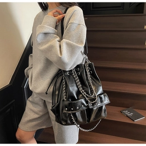 Detail of black glossy leather bucket bag featuring silver chains and rivet hardware