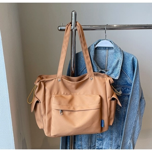 Detail of khaki nylon tote bag with front zip pocket and blue woven label on denim background