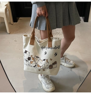 Detail of off-white canvas tote bag featuring cartoon cat prints and brown webbing handles
