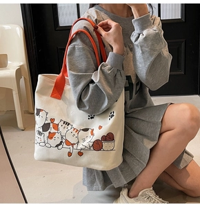 Detail of white canvas tote bag with orange handles and cute cartoon cat pattern