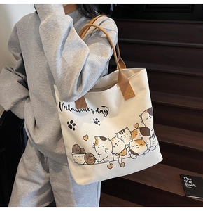 Close-up of cream canvas tote bag with cartoon cats print worn on shoulder