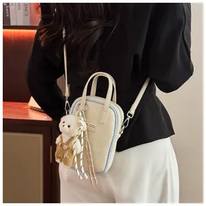 Detail of cream white pebbled leather crossbody bag with cute plush bear charm accessory