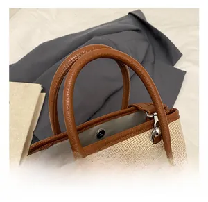 Detail of canvas tote bag with brown leather handles, magnetic closure and bow charm