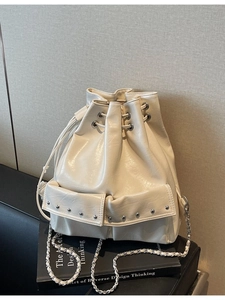 Creamy white drawstring bucket bag with silver studs and chain strap on a black sofa