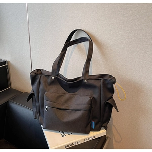 Macro shot of black nylon tote bag showing front zipper pocket and side drawstring detail