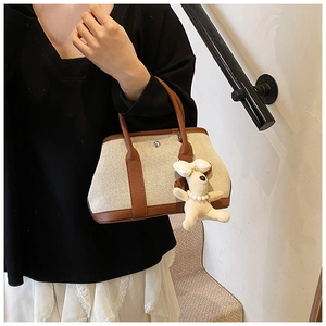 Detail of canvas tote bag with brown leather trim and cute white plush dog charm