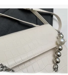 Detail of cream white saddle bag with crocodile texture, silver beads and pearl chain