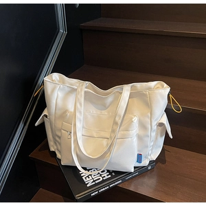Close-up of white canvas tote bag with side pockets and yellow drawstring on wood stairs