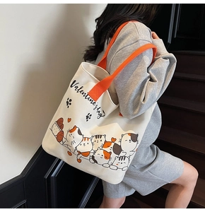 Close-up of canvas tote bag with orange handles and cute cartoon cat illustrations
