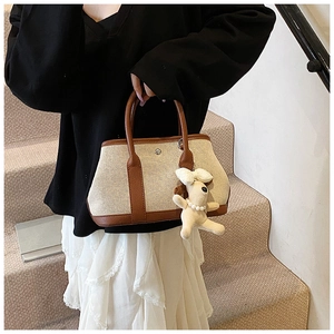 Detail of beige canvas tote with brown leather handles and plush dog charm on stairs