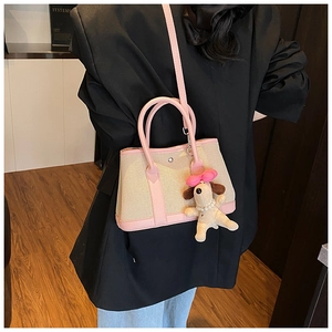 Model wearing a small beige canvas tote with pink leather straps and a plush puppy charm