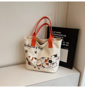 Detail of canvas tote bag with orange handles and cute cartoon cat illustrations