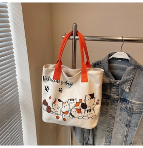 Detailed view of canvas tote bag with cartoon cat print and orange handles in a home setting