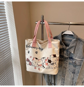 Detail view of cream canvas tote bag with pink straps and cute cartoon cat illustration