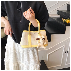Detail of canvas bucket bag with yellow trim and cute plush puppy charm accessory