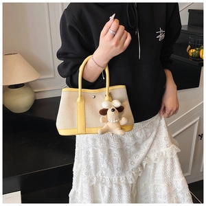 Detail view of canvas bucket bag with yellow leather handles and small dog plush charm