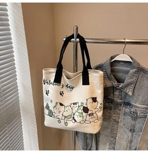 Detail of canvas tote bag with cat graphics and black handles hanging on a rack