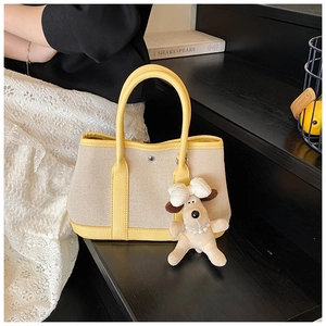 Close-up of yellow leather and beige canvas stitching with white puppy charm on tote bag