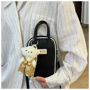 Detail of black lychee texture phone bag with white contrast edges and plush bear charm
