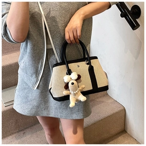 Detail of canvas tote with black leather trim and cute plush puppy charm accessory