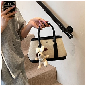 Detail of canvas tote bag with black leather trim and cute puppy plush charm pendant