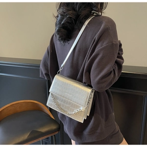 Detail of silver crocodile-embossed bag with metallic finish and pearl chain strap
