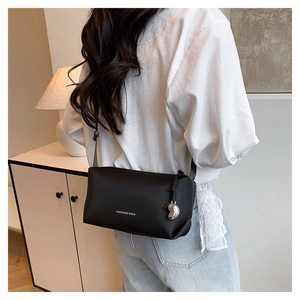 Détail d'un sac bandoulière noir avec logo blanc et pendentif en forme de cœur argenté