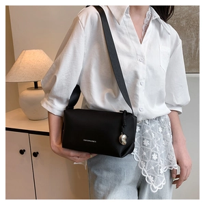 Détail d'un sac bandoulière noir mat avec sangle en nylon et breloque porté par un modèle
