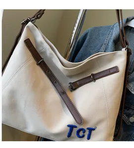 Detail of canvas tote bag featuring brown leather straps and blue TCT embroidery detail